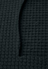 Svart textil med en strukturerad våffelmönster på ena sidan och slät tyg på den andra, vilket framhäver kontrasterande ytor.