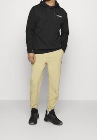 Sudadera negra con capucha y logo "TERBEX", combinada con pantalones amarillos claros y zapatillas deportivas negras con detalles rojos.