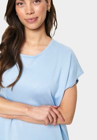 Top azzurro chiaro a maniche corte realizzato in tessuto a coste, con collo rotondo e vestibilità morbida, caratterizzato da bordi arrotolati alle maniche.