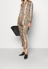 Ormskinnsmönstrad tvådelad outfit bestående av en knäppt skjorta och smala byxor i nyanser av brunt och beige, ihop med svarta skor och handväska.