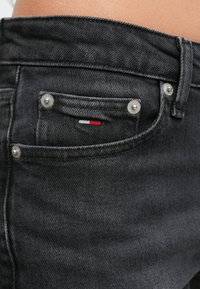 Čierne džínsy z denimu s úzkym strihom, striebornou kovovou výbavou a malou nášivkou s logom v červenej, bielej a modrej farbe na zadnom vrecku.