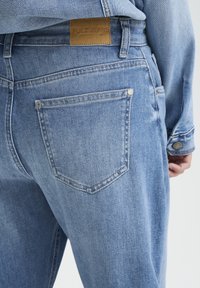 Svetlomodré riflové nohavice s textúrovaným povrchom, ktoré majú hnedú koženú značku s nápisom „PULZ JEANS“, dvojité zadné vrecká a strieborné nitmi.