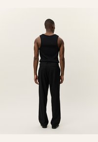 Black sleeveless tank top made of knit fabric, paired with black trousers. The outfit is simple, with a relaxed fit and minimal design.