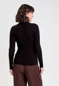 Sort ribbet langærmet top med høj krave, der har et tætsiddende design. Bagsiden er glat med en let stræk og en længde til hoften.