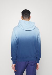 Sudadera con efecto ombre azul, fabricada en una suave mezcla de algodón, con mangas largas y capucha con cordón, que va de un azul claro a un azul oscuro.