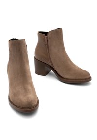 Paire de bottines en daim marron avec fermeture éclair latérale et talons blocs, présentées sur un fond blanc.