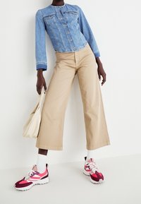 Džínová bunda se zacvakávacími knoflíky, světle modrá, dvě náprsní kapsy; béžové široké kalhoty; vícebarevné tenisky s růžovými, červenými a bílými akcenty, bílé ponožky.