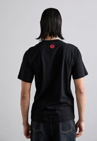 Svart bomull T-skjorte med rund hals og kort erm; rød grafisk detalj bak. Båret med mørk denim jeans.