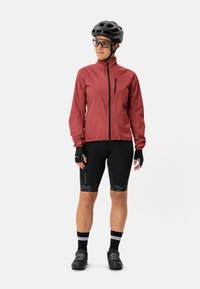 Rode lichtgewicht fietsjack, zwarte gevoerde shorts met een subtiel patroon, zwarte helm, handschoenen en fietsschoenen; ontworpen voor prestaties.