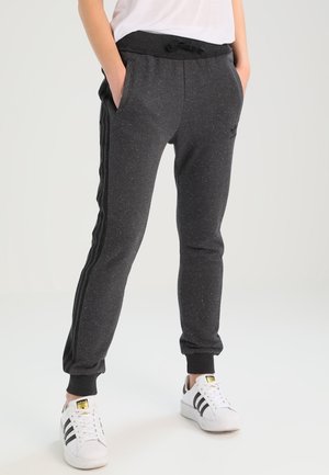 Persoon draagt donkergrijze joggingbroek met zwarte zijstrepen en witte Adidas-sneakers met zwarte strepen.