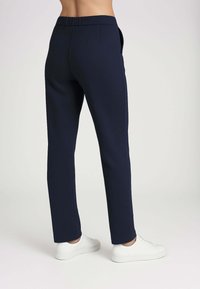 Pantaloni tapered blu navy realizzati in tessuto morbido con vita regolabile, dotati di tasche laterali e una texture liscia. Abbinati a sneakers bianche.