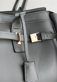 Grijze leren handtas met gouden hardware, gestructureerde vorm, stikdetails en een riemband met een gesp.