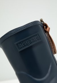 Bota de goma azul marino con una parte superior texturizada, logo de la marca en relieve y un detalle de cuero marrón con un lazo para facilitar su puesta.