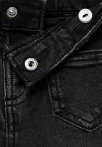 Črnen denim blago z teksturirano površino, ki ima srebrno kovinsko zapiranje na gumb in majhen žep z natančnim šivanjem.