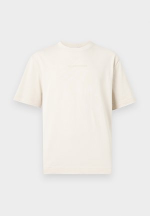 Camiseta de manga corta color crema con cuello redondo y logo en relieve sutil en el pecho, mostrada sobre un fondo gris claro.