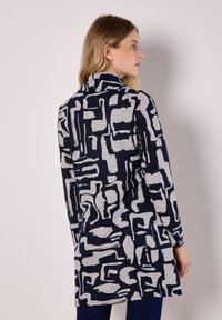 Túnica de manga larga y cuello alto en patrón azul marino y gris. Presenta formas abstractas, tejido suave y un ajuste relajado, que llega hasta la mitad del muslo.
