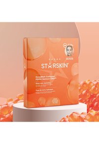 Oranje doos van Starskin DeepMelt Collagen PDRN Salmon DNA hydraterende gezichtsmaskers tentoongesteld op een wit voetstuk met oranje gelachtige bolletjes.