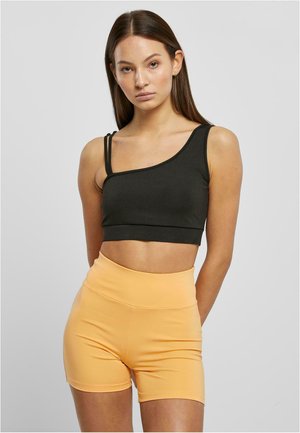 Sort crop top med asymmetrisk design og to tynde stropper, parret med højtaljede, tætsiddende orange shorts. Blødt, strækbart stof.