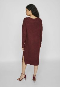 Robe tricotée bourgogne à manches longues, à col rond, avec des fentes latérales et une coupe décontractée. Portée avec des sandales à talons hauts bordeaux.
