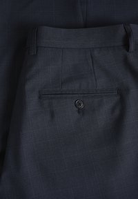 Pantalones de cuadro azul marino hechos de tela texturizada, con un bolsillo trasero con cierre de botón y un diseño de frente plano.