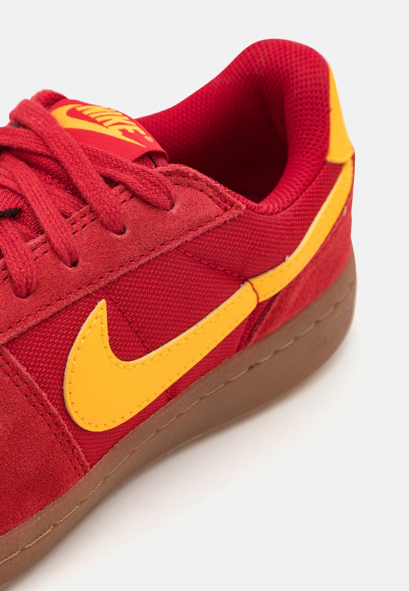 Zapatillas rojas de ante y malla con acentos amarillos, que cuentan con un prominente swoosh amarillo de Nike y una suela de goma marrón.