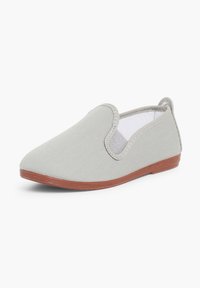 Chaussure à enfiler gris clair avec semelle marron, panneaux latéraux élastiques et petite boucle au talon, présentée sur fond blanc.