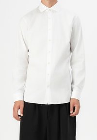 Camicia bianca a maniche lunghe con colletto classico, realizzata in tessuto liscio, con una leggera lucentezza e orlo dritto.