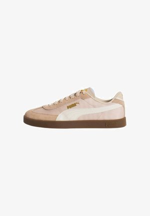 Zapatillas Puma con un upper de gamuza y tela en un tono beige claro, acentos blancos, diseño con cordones y una suela de goma marrón.