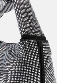 Černá kabelka s řadami stříbrných kamínků, s měkkým tkaninovým tělem a elegantním designem. Pevná rukojeť pro snadné nošení.