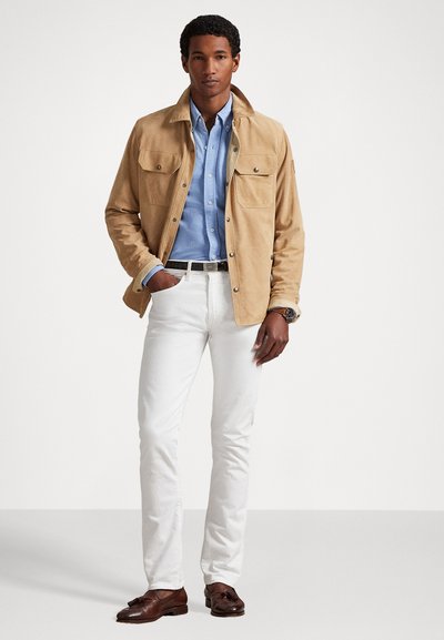 Καφέ σουέτ τζάκετ με τέσσερις μπροστινές τσέπες, σε συνδυασμό με πουκάμισο ανοιχτού μπλε, λευκά παντελόνια και καφέ δερμάτινα παπούτσια. Απλός, κομψός σχεδιασμός.