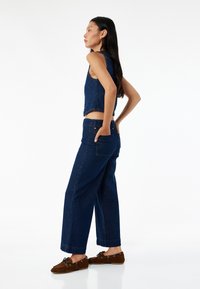 Denim cropped top yhdistettynä leveisiin tummansinisiin farkkuihin. Asusteessa on taskut ja yhtenäinen väri, hienovaraisilla ompeluyksityiskohdilla.
