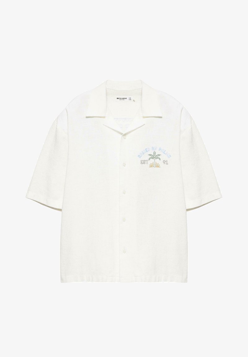 Chemise blanche à manches courtes avec boutons et col, avec un petit motif de palmier et le texte « EST 91 » sur la poitrine gauche.