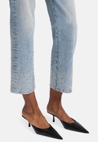 Jeans in denim azzurro chiaro con strass sparsi sull'orlo, abbinati a mules nere eleganti con punta a stiletto.