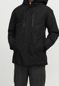 Svart, isolerad huva jacka med två vertikala dragkedjefickor, rak passform och justerbara snoddar för huvan.