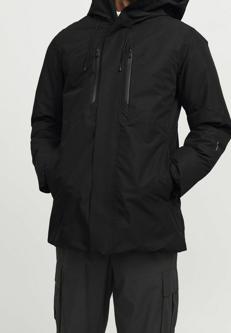 Svart, isolerad huva jacka med två vertikala dragkedjefickor, rak passform och justerbara snoddar för huvan.