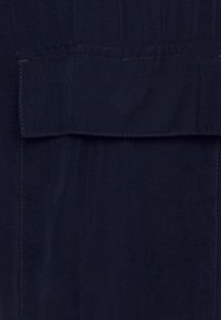 Tecido azul marinho com uma textura suave, apresentando um bolso horizontal na parte superior e costuras proeminentes ao longo das bordas.