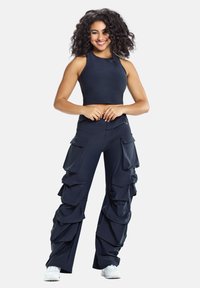 Merihenkinen crop top ilman hihoja yhdistettynä merihenkisiin cargo-housuihin, joissa on useita suuria taskuja ja kerättyjä kankaita.