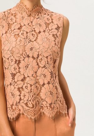 Haut sans manches en dentelle pêche avec motif floral et bords festonnés porté avec un pantalon pêche assorti.