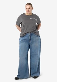 Gray t-shirt with "HOLLYWOOD" text paired with wide-leg blue denim jeans. The jeans have a faded wash and a loose fit, featuring side pockets.