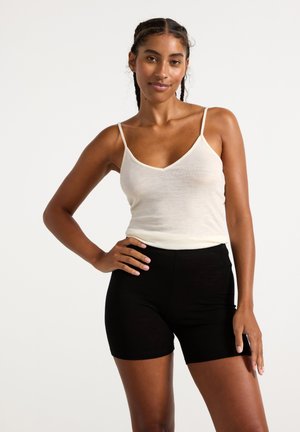 Lichtbeige spaghetti straps top met een v-hals, gecombineerd met zwarte shorts met een hoge taille. Soepele textuur op beide kledingstukken.