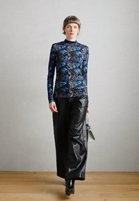 Langärmliges Oberteil mit einem mehrfarbigen Blumenmuster auf dunklem Hintergrund, kombiniert mit hochtaillierten schwarzen Lederhosen.