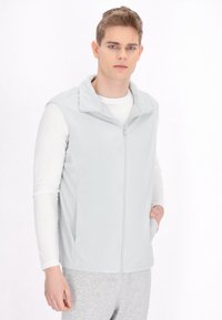 Hellgraue Fleece-Weste mit Reißverschluss auf der Vorderseite, hohem Kragen und Seitentaschen, getragen über einem weißen Langarmshirt und grauen Hosen.