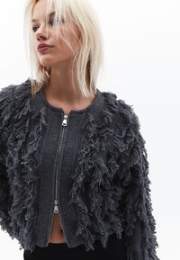 Grå stickad jacka med en texturerad fransdesign. Har rund halsringning, dragkedjestängning och ribbade ärmslut.