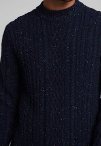 Granatowy sweter z warkoczykami, z wysokim dekoltem, teksturowanym wzorem i wielokolorowymi plamkami na całej tkaninie.