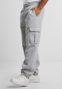Grå bomullscargobyxor i sweatpants stil med resårmidja, sidofickor och en lapplicka på låret, kombinerat med vita sneakers.