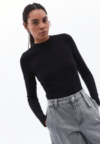 Top nero a maniche lunghe con colletto alto, design aderente, abbinato a pantaloni grigi chiari con texture, dotati di tasche e chiusura con bottone.
