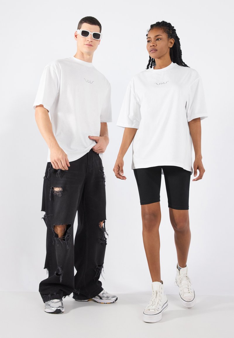 Baltie oversize T-krekli, melni nolietoti džinsi un melni velosipēdistu šorti. Modelis valkā baltas kedas un saulesbrilles. Gluda auduma, brīva piegriezuma.
