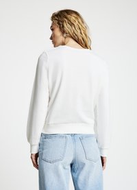 Weißes, leichtes Sweatshirt mit rundem Ausschnitt, gerippten Bündchen und Saum. Kombiniert mit hellblauen, locker sitzenden Jeans. Einfaches Design, keine Muster.