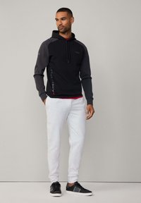 Sudadera con capucha negra y gris con un acento rojo, combinada con pantalones de chándal gris claro y zapatillas negras. Diseño de ropa deportiva casual.
