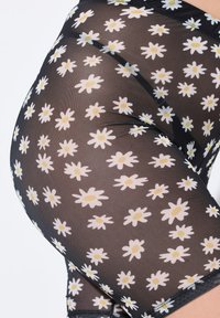 Pantaloni corti in tessuto nero trasparente con stampa di margherite bianche e gialle. Il design presenta una texture liscia e una forma aderente con rifiniture in pizzo.